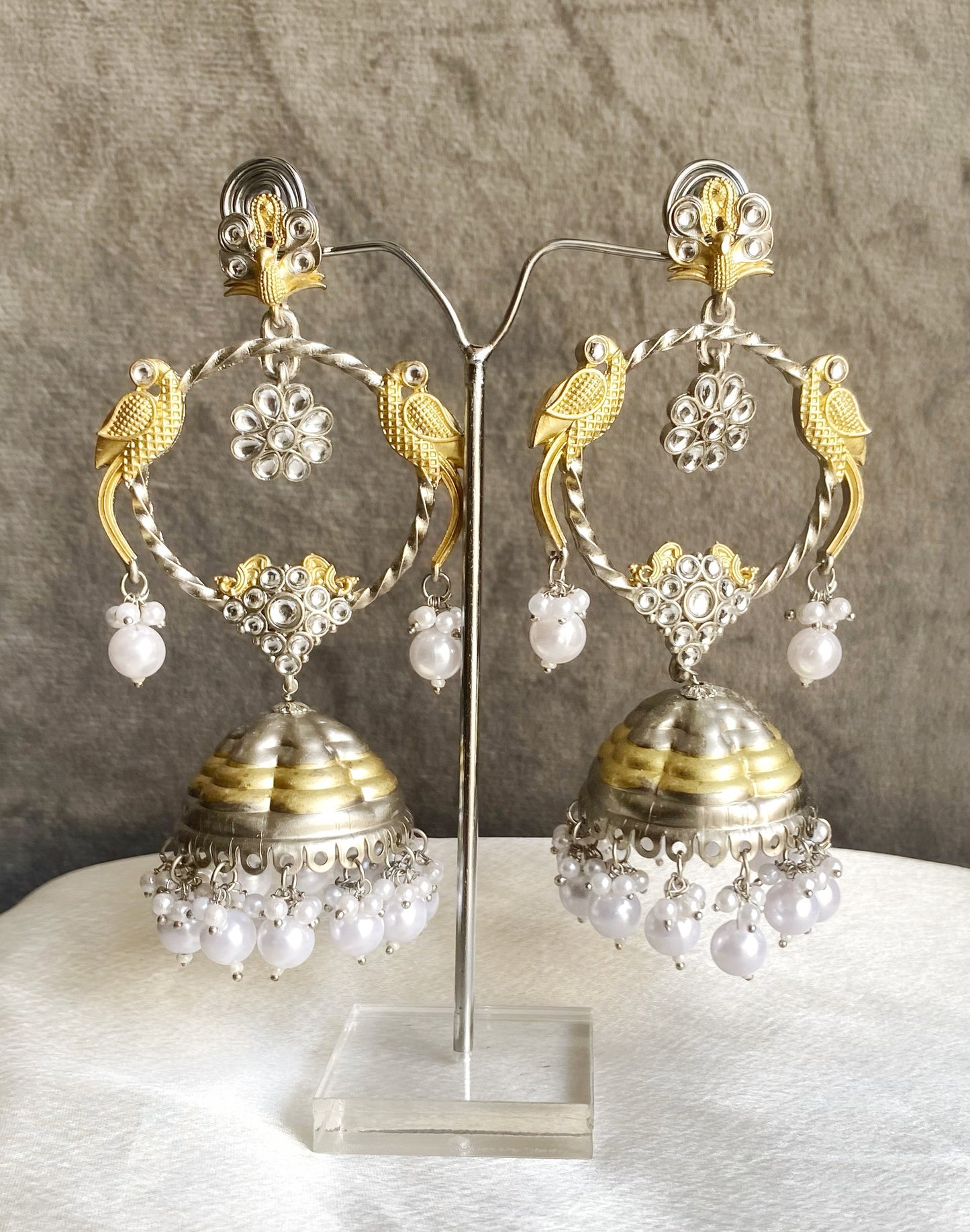 Pair of gold and silver earrings with pearl-like beads on a gray background