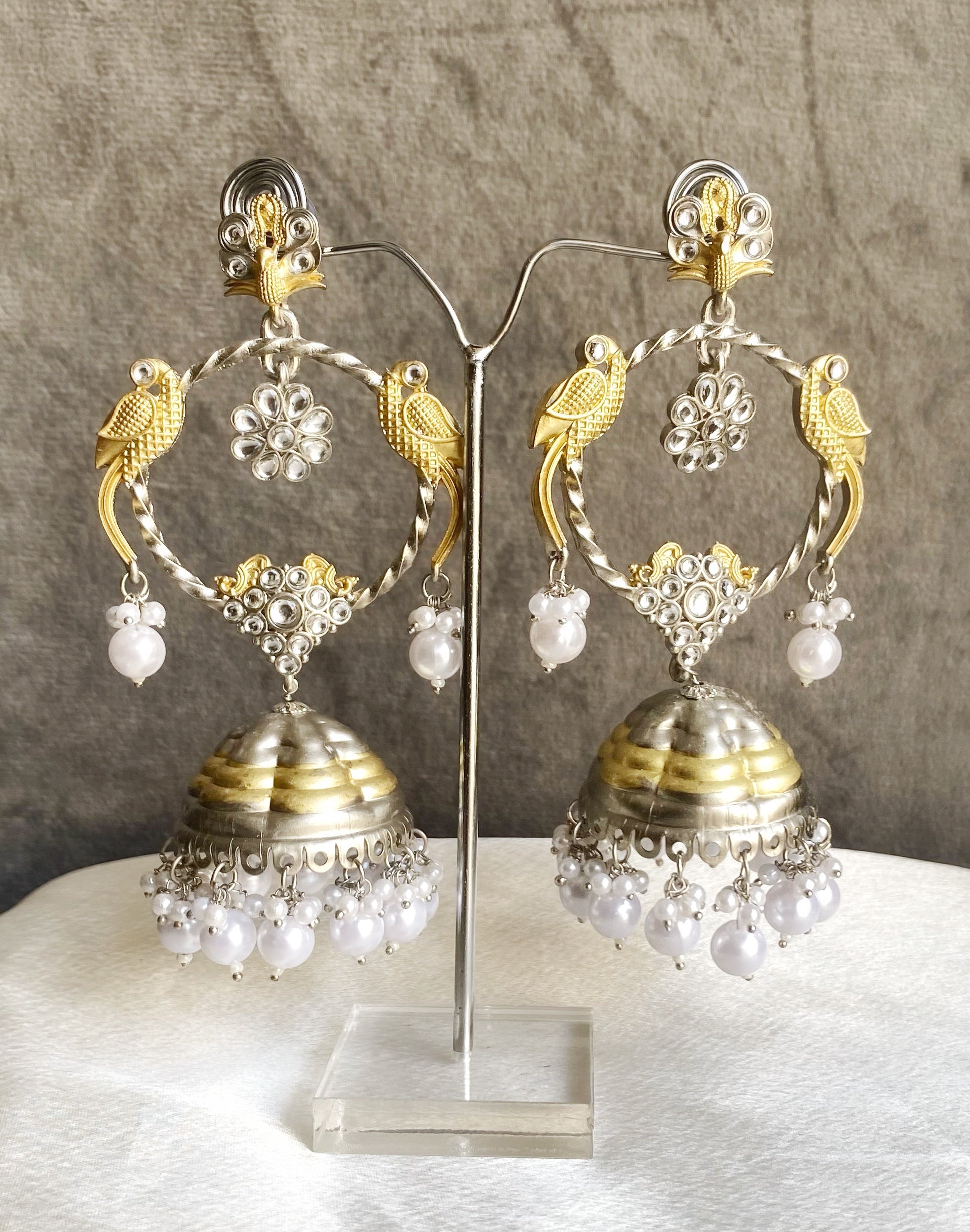 Pair of gold and silver earrings with pearl-like beads on a gray background